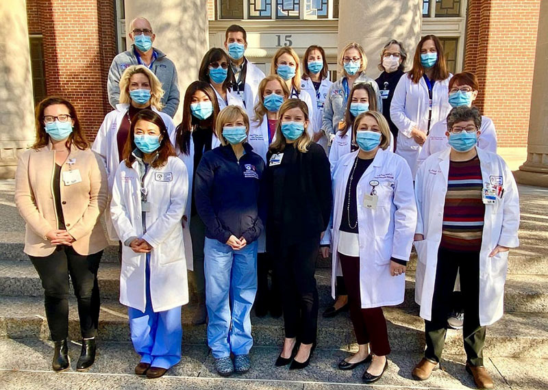 A group of 19 medical professionals in masks standing in front of a building