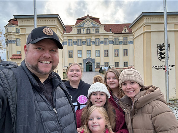 A patient with her husband and four kids in a selfie with a building in the background