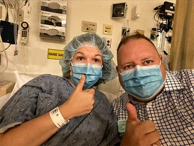 A patient and her husband in masks showing their thumbs up
