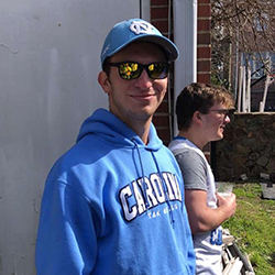 A male student wearing a cap and jacket in carolina blue colors