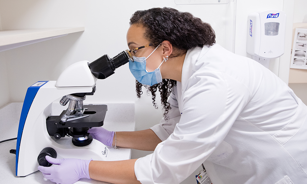 female clinician looking into microscope